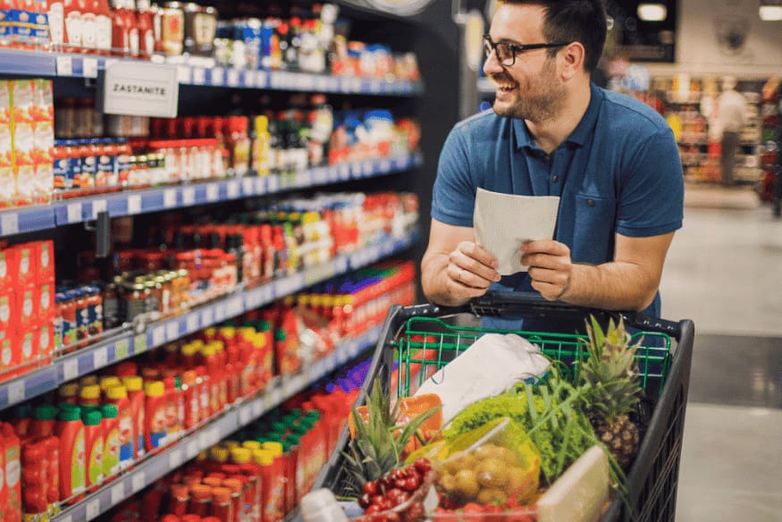 Persona en el supermercado usando una lista para planificar compras del hogar de forma eficiente