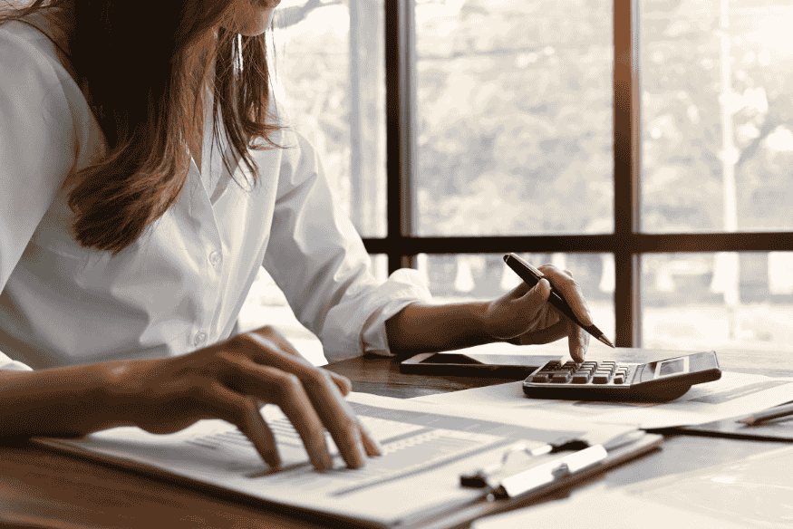 Mujer haciendo cálculos con calculadora y documentos financieros en escritorio.
