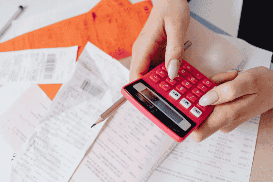 Manos usando una calculadora sobre facturas para calcular pequeños gastos recurrentes