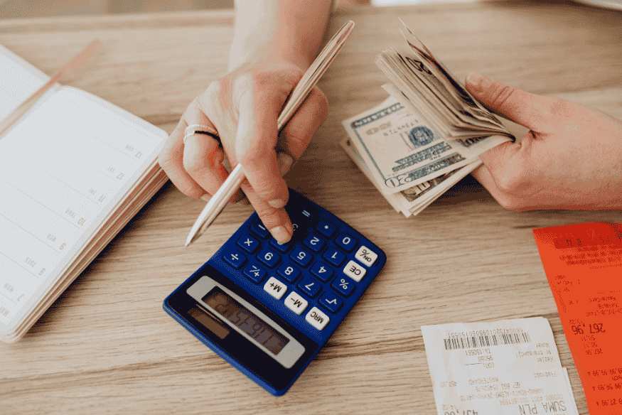 Manos usando calculadora con dinero y recibos para calcular el precio por unidad de productos