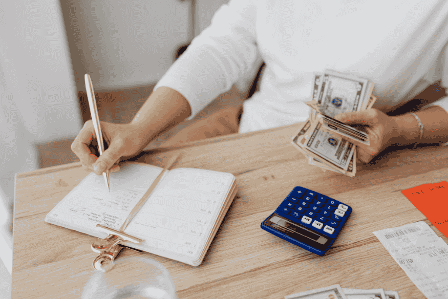 Persona anotando gastos y contando dinero para planificar vacaciones sin deudas